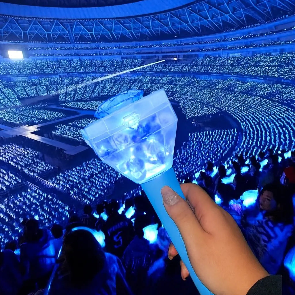 Fan tenant le Treasure Lightstick lors d’un concert K-pop, avec un stade illuminé par des lightsticks officiels bleus